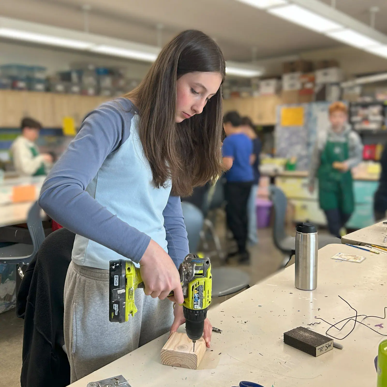 Lucille is drilling holes into a block of wood which will become the base of a Modern Art sculpture.